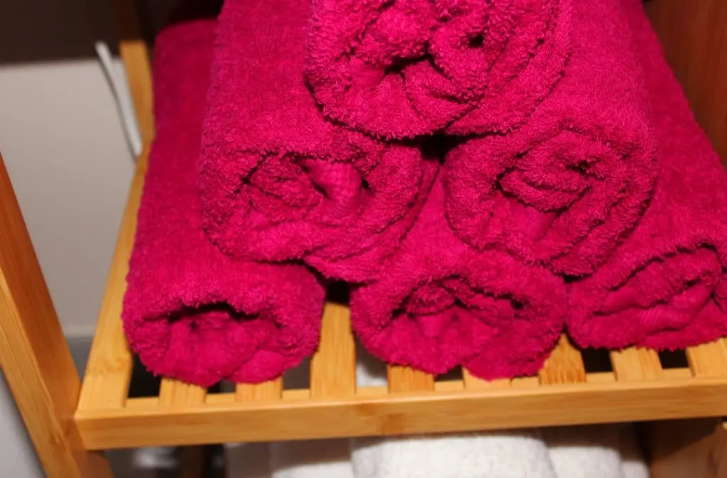 Dieses Bild zeigt einen Stapel roter Handtücher. Diese liegen gestapelt auf einem Regal. Darunter sind weiße Handtücher zu sehen. Dieses Element dient der Dekoration des Massageraums in der Massageoase im Ergomar Ergolding bei Landshut.